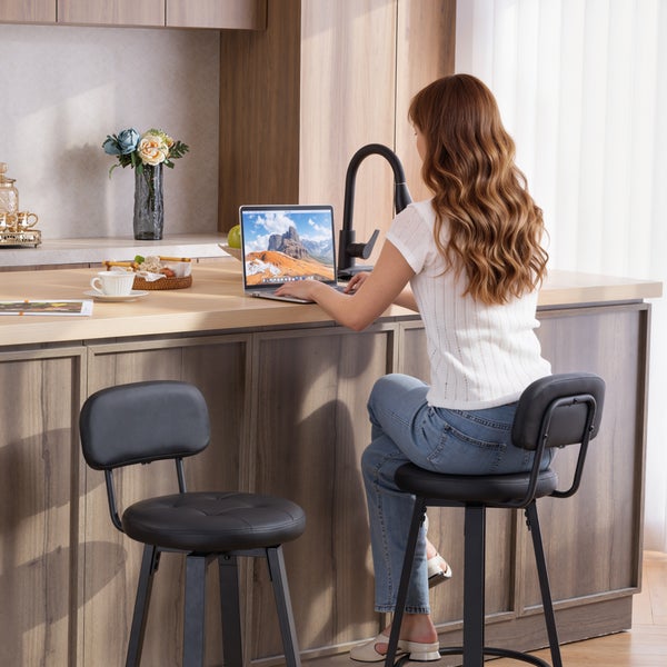 Küchenszene mit einer Frau, die an einem Küchentresen sitzt und einen Laptop benutzt, und zwei Barhockern