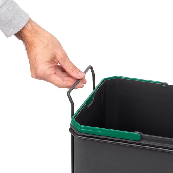 Eine Hand hebt einen schwarzen Mülleimer-Einsatz mit Metallbügel und grünem Rand hoch.