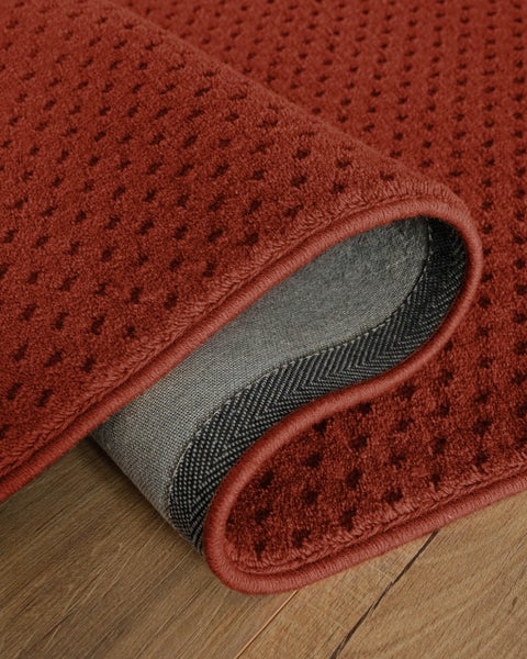 Strukturierter roter Teppichläufer mit geometrischem Muster und Kettelrand auf einem Holzboden.