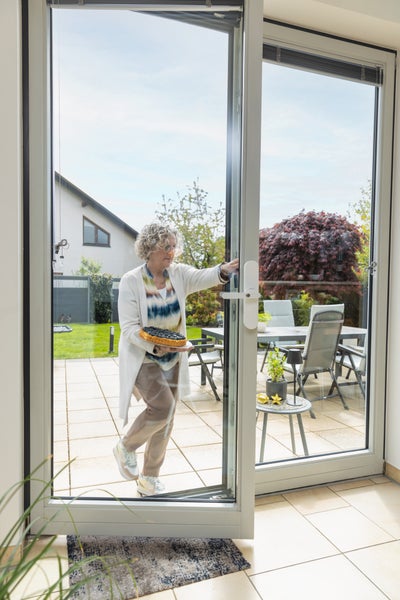 Weiße Balkontür aus Kunststoff und Glas, die einen fließenden Übergang zwischen hellem Innenraum und gepflasterter Terrasse mit Gartenmöbeln schafft.