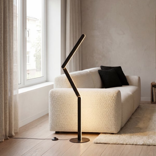 Moderne schwarze Zickzack LED-Stehleuchte in einem hellen Wohnzimmer neben einem hellen Sofa mit schwarzen Kissen und einem Teppich.