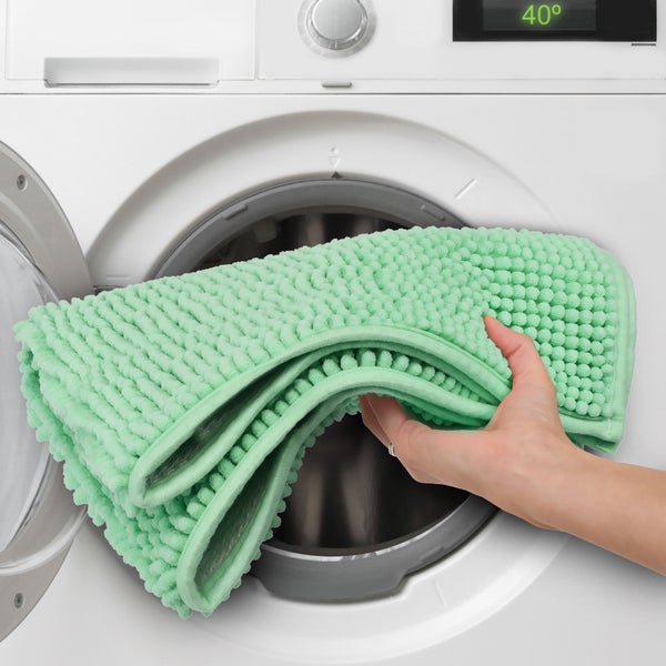 Eine Person legt eine Badematte zum Waschen in eine Waschmaschine.