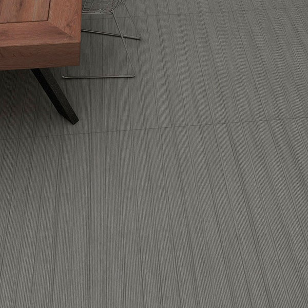 Großformatige Bodenfliese in Holzoptik mit feiner Oberflächenstruktur, verlegt in einem Wohnbereich mit Holztisch und Metallstuhl.