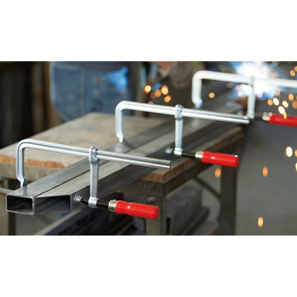 Drei Schraubzwingen fixieren ein Metallstück auf einem Werktisch beim Schweißen.