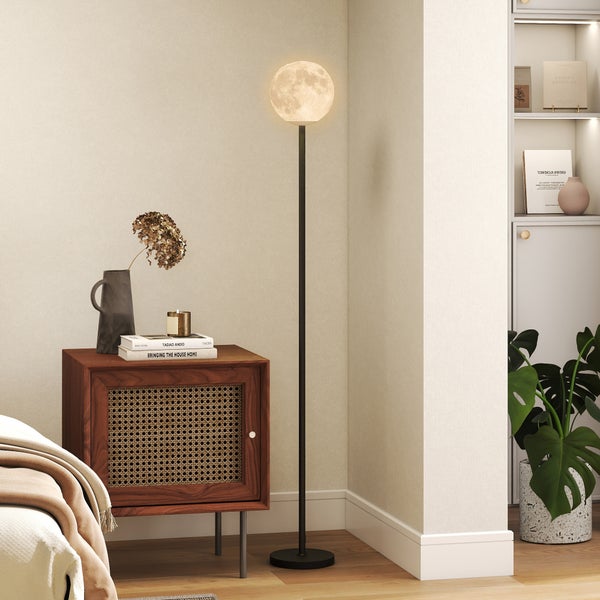 Innenaufnahme eines Raumes mit einem Nachttisch, einer Stehlampe und einem Bücherregal.