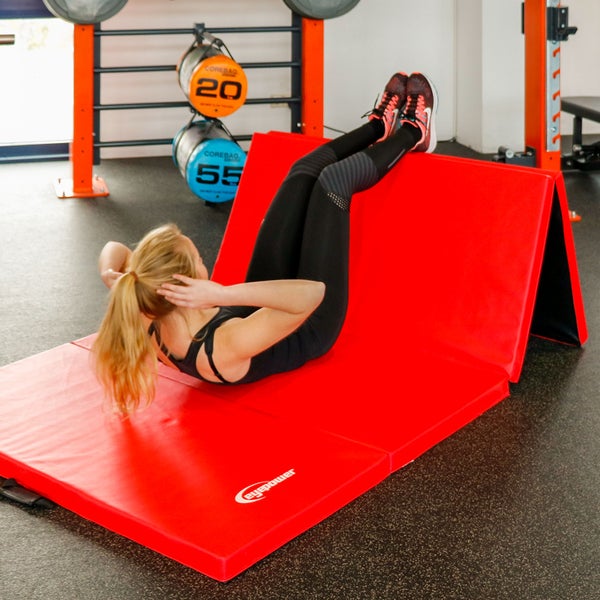 Frau trainiert Bauchmuskeln auf einer roten Bauchmuskelbank in einem Fitnessstudio.