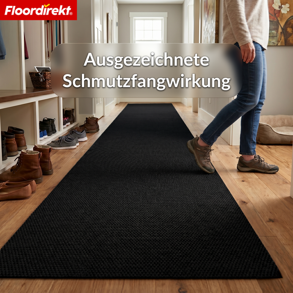 Langer schwarzer Schmutzfangläufer mit ausgezeichneter Schmutzfangwirkung in einem hellen Flur mit einer Person. Floordirekt Logo.