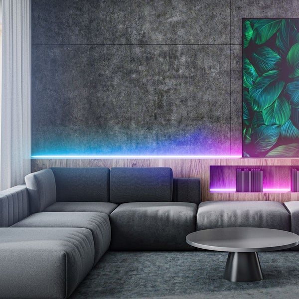 Modernes Wohnzimmer mit grauem Ecksofa, Betonwand und farbigem LED-Streifen in Blau und Lila für stimmungsvolle Akzentbeleuchtung.