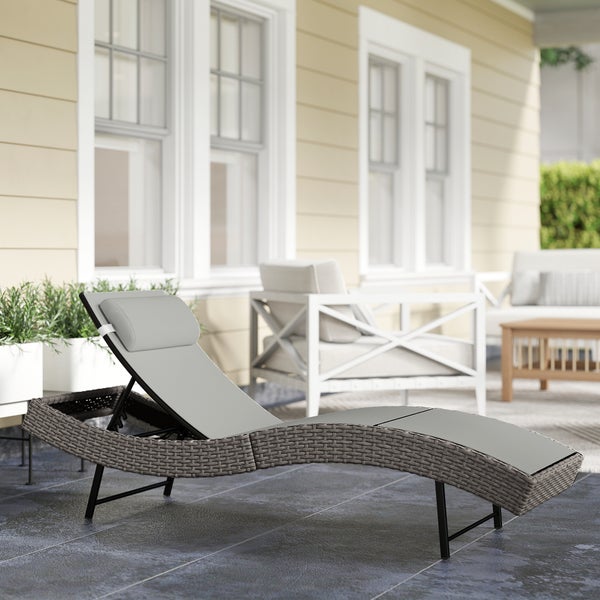 Ergonomische Sonnenliege aus Geflecht mit Polsterauflage auf einer Terrasse mit Gartenmöbeln.