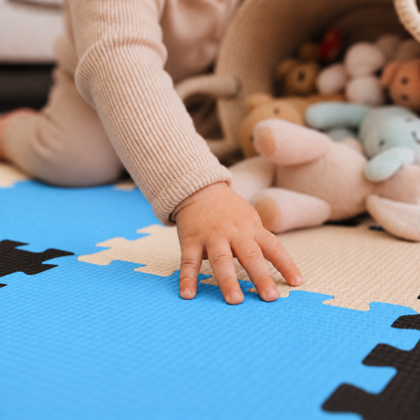 Kind spielt auf einer Puzzlematte aus Schaumstoff mit strukturierter Oberfläche neben einem Korb voller Stofftiere