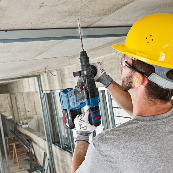 Ein Bauarbeiter bohrt mit einem Akku-Bohrhammer ein Loch in die Betondecke.