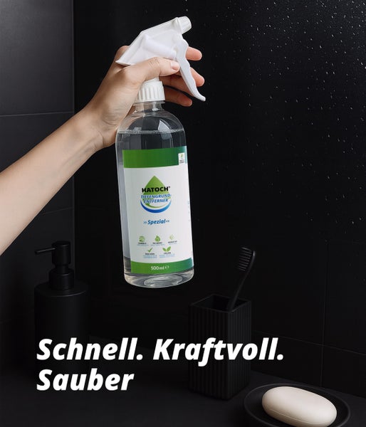 Eine Hand hält eine Sprühflasche HATOCH Tiefengrundentferner Spezial vor einem Badezimmer.