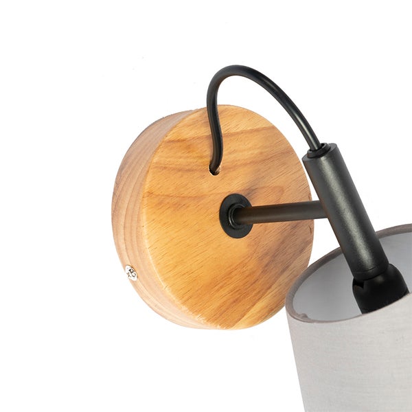 Wandleuchte mit rundem Holzfuß, schwarzem Metallarm und grauem Stoffschirm in der Nahaufnahme.