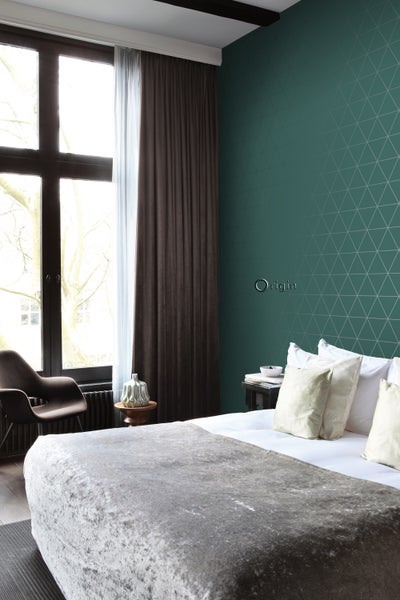 Schlafzimmer mit Bett, Vorhängen und geometrischer Tapete für ein modernes Ambiente.