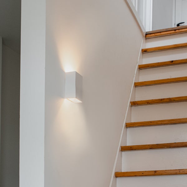 Weiße Wandleuchte neben einer Treppe im Innenraum.