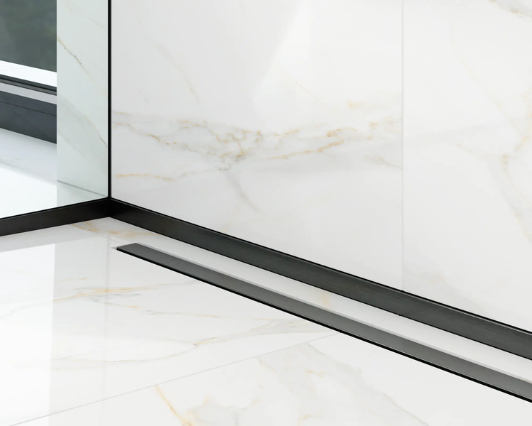 Duschrinne und Eckprofil in Schwarz auf hellen Marmorfliesen im Badezimmer.