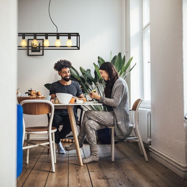 Moderne schwarze Pendelleuchte fünf-flammig über einem Esstisch in hellem Esszimmer mit großen Zimmerpflanzen.