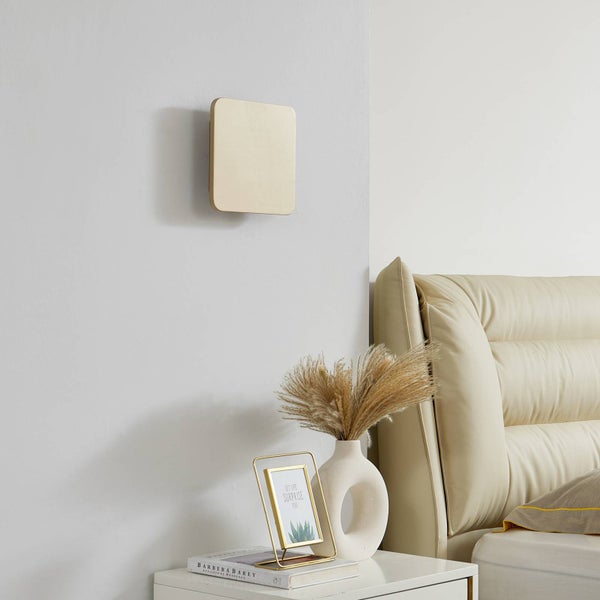 Quadratische goldene Wandleuchte im Schlafzimmer über einem Nachttisch mit Pampasgras-Dekoration und einem gepolsterten beigen Kopfteil.