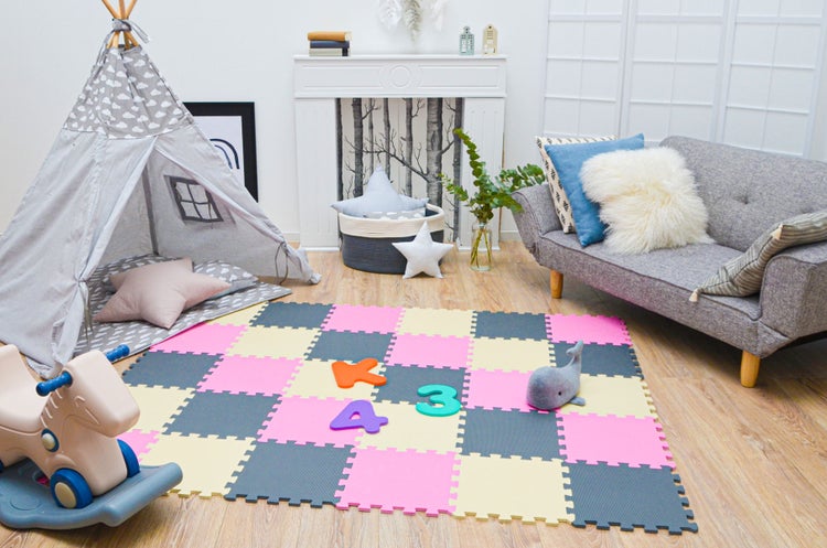 Helles und organisiertes Kinderzimmer mit einer Puzzle-Spielmatte, einem Tipi-Zelt, einem Schaukelpferd, einem grauen Sofa und einem Kaminsims.