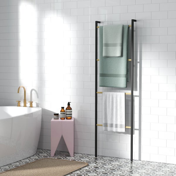 Modernes helles Badezimmer mit einer Handtuchleiter aus Metall und Holz an einer Fliesenwand neben einer Badewanne mit goldener Armatur.