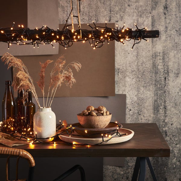 Dekorativer Tisch mit Holz, Vasen, Nüssen, Trockenblumen und Lichterkette