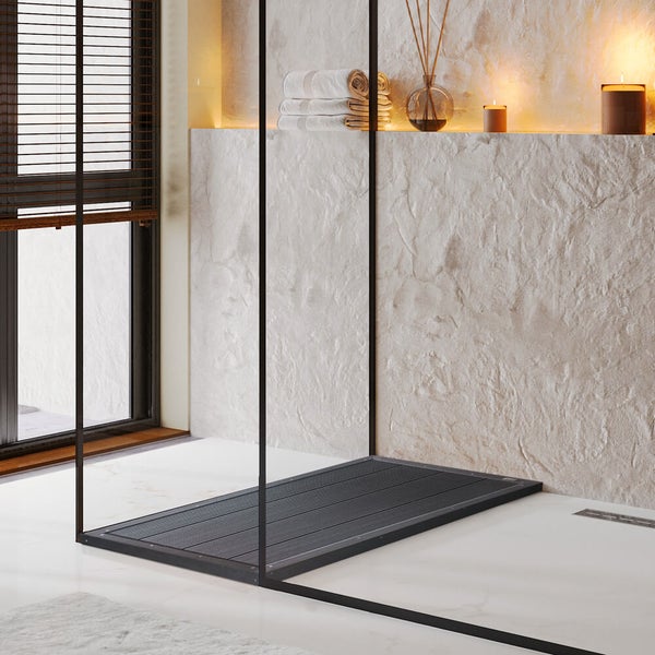 Ebenerdige Dusche mit schwarzen Glasprofilen und einer dunklen Duschfläche vor einer hellen Steinwand mit Handtüchern und Kerzen.