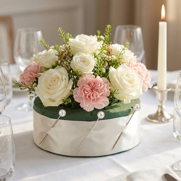 Rundes Blumengesteck aus weissen und rosa Rosen mit Steckschwamm auf einem festlich gedeckten Tisch mit Kerze.