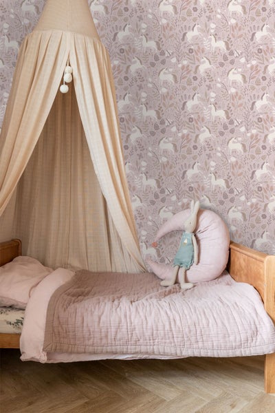 Kinderzimmer mit gemusterter Einhorntapete, einem Holzbett mit Baldachin, rosa Bettwäsche und einem dekorativen Mondkissen.