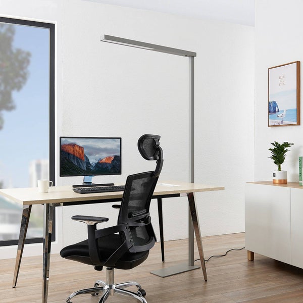 Modernes Homeoffice mit minimalistischer silberner Stehleuchte über hellem Schreibtisch, ergonomischem Bürostuhl und hellem, geordnetem Ambiente.
