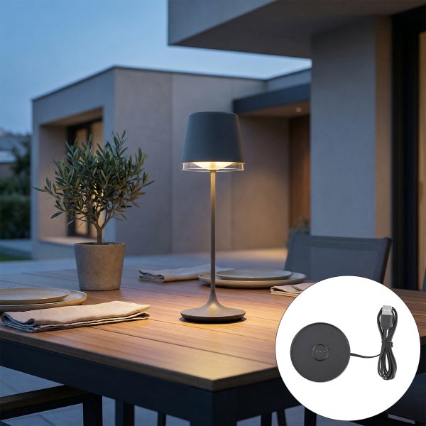 Dunkelgraue kabellose Tischleuchte auf hölzernem Gartentisch, organisierte Atmosphäre mit Tellern, Pflanze und Ladestation.
