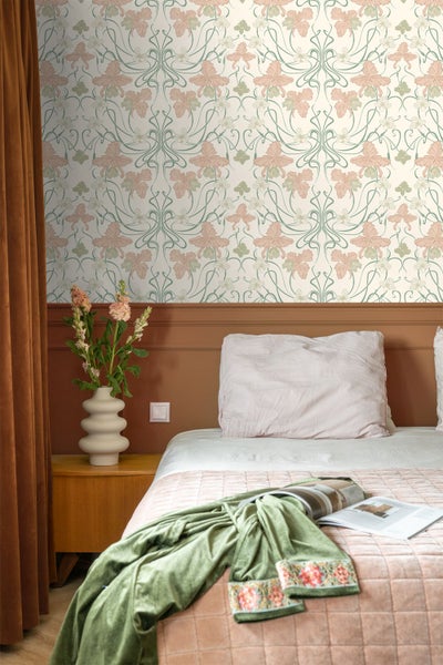 Schlafzimmer mit floraler Jugendstil-Tapete, Wandpaneele, einem Bett mit Decken und einem Nachttisch mit Vase.