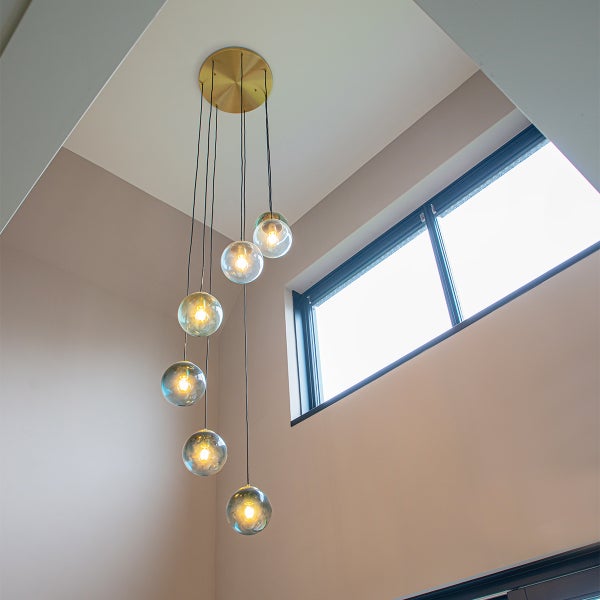 Moderne Pendelleuchte mit sechs Glaskugeln in verschiedenen Höhen hängend und runder Deckenhalterung in einem Wohnraum.