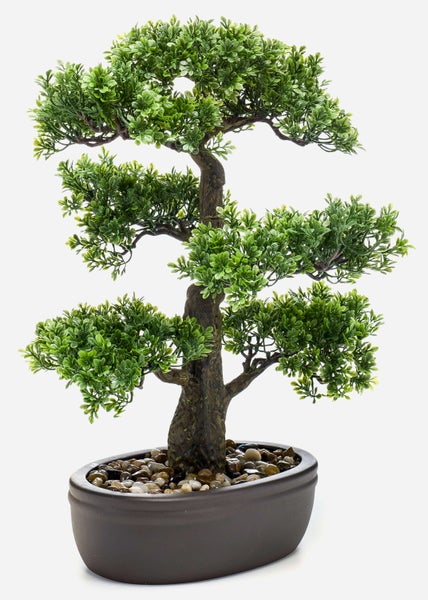 Künstlicher Bonsai mit grünen Blättern in einer dunklen ovalen Schale mit dekorativen Kieselsteinen.