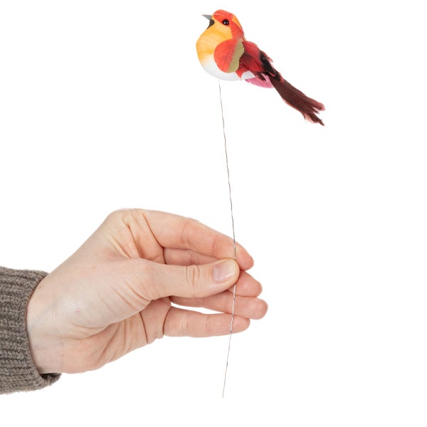 Roter und gelber Dekovogel am Draht, kleiner künstlicher Vogel als Blumenstecker mit echten Federn, von einer Hand gehalten.