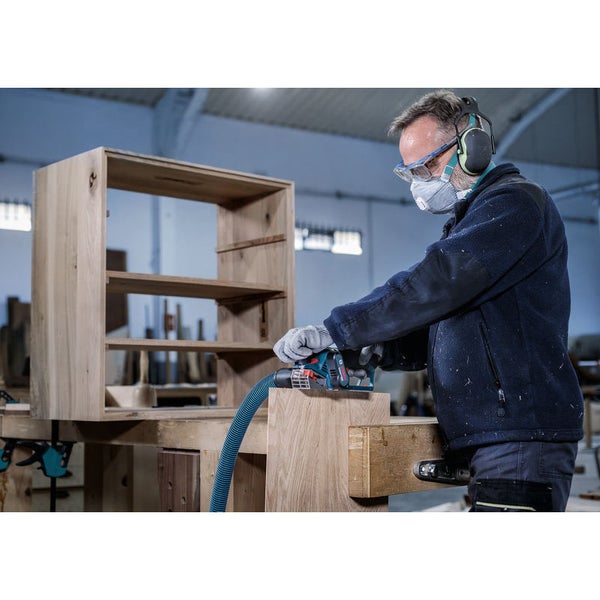 Ein Mann schleift Holz mit einem Schleifgerät, trägt dabei Sicherheitsausrüstung wie Schutzbrille, Gehörschutz und Staubmaske.