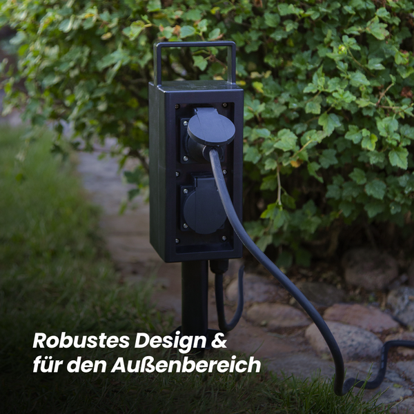 Außensteckdose mit zwei Steckdosen und einem angeschlossenen Kabel im Garten.