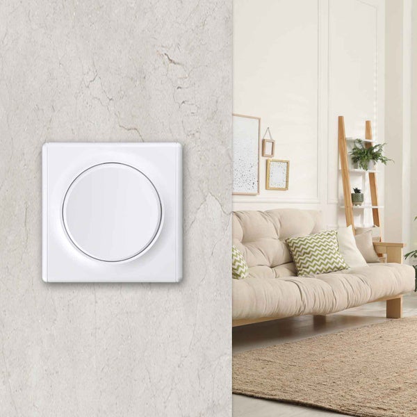 Ein moderner Lichtschalter mit rundem Einsatz an einer strukturierten Wand neben einem hellen Wohnzimmer mit Sofa und Holzregal.