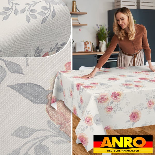Eine Frau legt eine abwaschbare Tischdecke mit Rosenmuster in einer hellen Küche auf, inklusive Detailansicht der Struktur und ANRO Deutsche Manufaktur Logo.