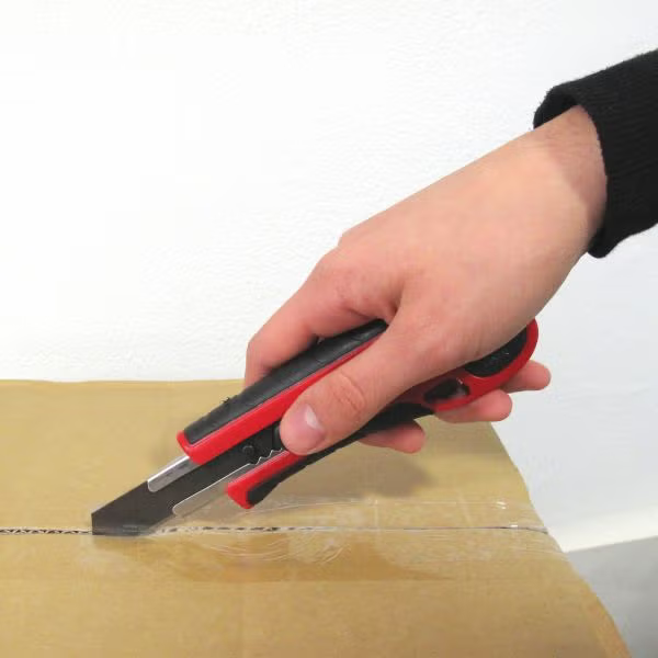 Eine Hand schneidet mit einem Cuttermesser ein Paket aus Pappe auf.