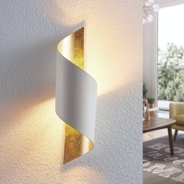 Moderne Wandleuchte in geschwungener Form, außen weiß und innen goldfarben, an einer weißen strukturierten Wand im Wohnzimmer.