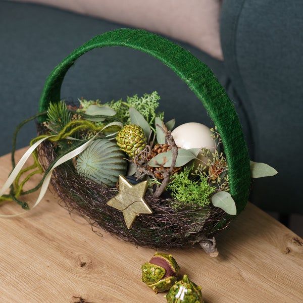 Dekoratives Osternest mit Grünpflanzen, Ei und Stern auf einem Holztisch