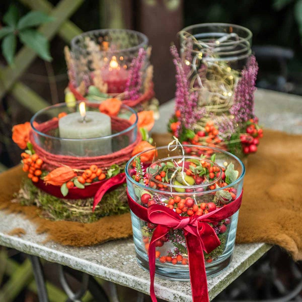 Herbstliche Tischdekoration mit Kerzengläsern, Beeren, Heidekraut und Lichterketten auf einem steinernen Gartentisch.