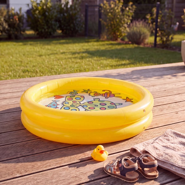 Aufblasbares Planschbecken für Kinder mit bedrucktem Boden auf einer Holzterrasse, inklusive Badeente und Kindersandalen.