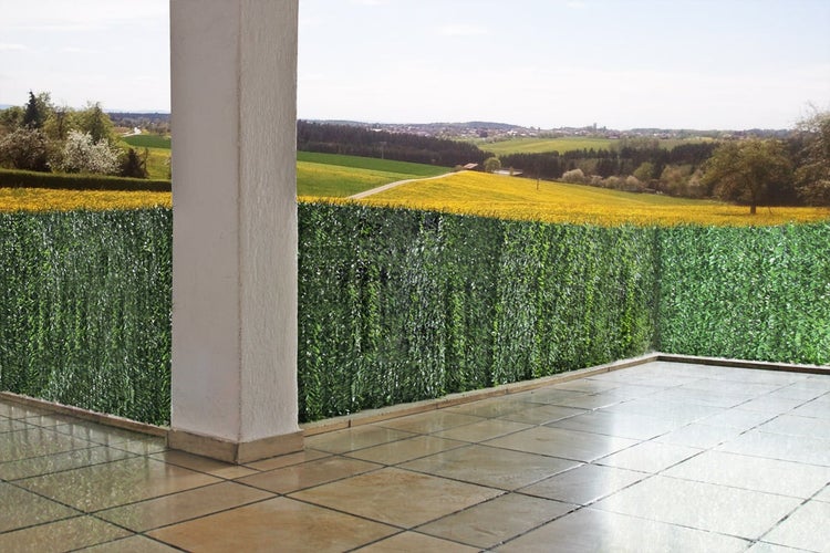 Balkon mit künstlicher Hecke und Ausblick auf eine grüne Landschaft
