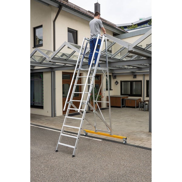 Eine Person steht auf einer Aluminium Rollgerüstleiter bei Wartungsarbeiten an einer Terrassenüberdachung aus Metall und Glas.