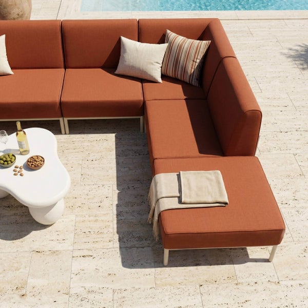 Moderne Gartenlounge-Ecke mit rostfarbenen Polstern auf einer Steinterrasse am Pool. Inklusive organisch geformtem Couchtisch und Hocker.