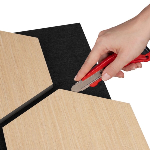 Eine Hand schneidet die schwarze Rückseite eines sechseckigen Wandpaneels mit einem Cuttermesser zu.