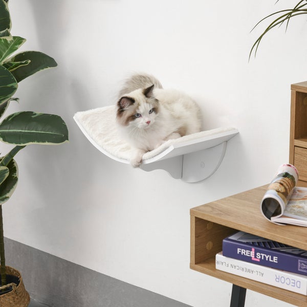 Modernes, weißes Wand-Katzenbett mit gebogener Liegefläche und flauschiger Einlage in einem hellen, aufgeräumten Zimmer.