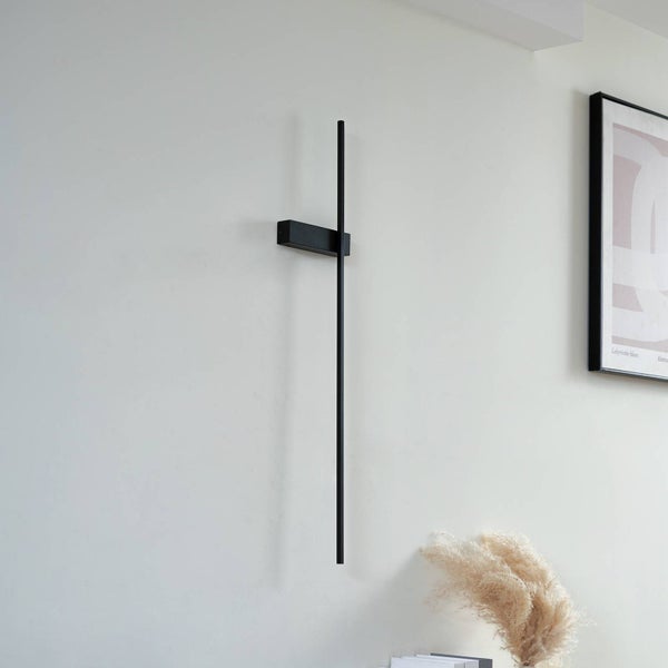 Moderne schwarze LED-Wandleuchte im minimalistischen Stab-Design in einer hellen Wohnumgebung.