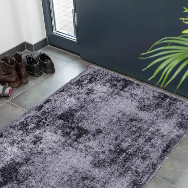 Eine rechteckige, flauschige Fußmatte mit marmoriertem Design im Eingangsbereich vor einer Tür mit Schuhen auf Fliesen.